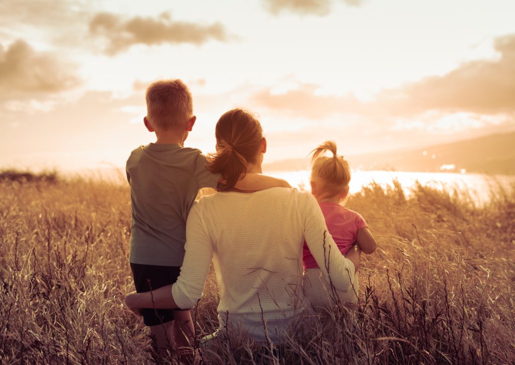 Mother and her two children sitting together in a field looking out to the sunset