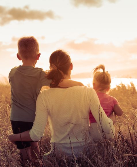 Mother and her two children sitting together in a field looking out to the sunset