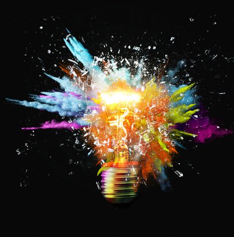 Creative light bulb explodes with colorful paint splashes and shards of glass on a black background. Think differently creative idea concept. Dry paint splatter. Brainstorm and think